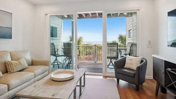 A modern living room with a sofa, coffee table, and a dining area with chairs and a table. - Oceanfront Oasis (Tybee Island)