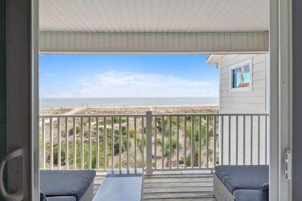 A balcony with a view of the beach, a wooden deck, and a small seating area.