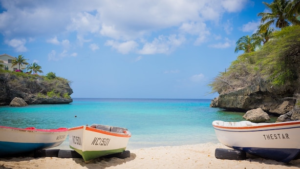 Drei Boote namens MERCHO, AC-501 und THESTAR an einem sandigen Strand mit klarem türkisblauem Wasser und felsigen Klippen.