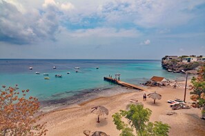 A beach with boats, a pier, and a small building with a thatched roof.