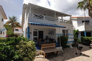 Un edificio de dos plantas con un balcón, un patio con un banco de madera y una parrilla para barbacoa.