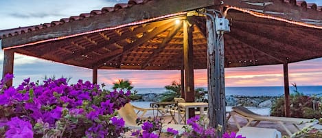 Un espacio de estar al aire libre cubierto con vista al océano al atardecer.