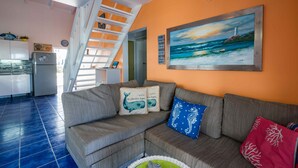 Ein Wohnzimmer mit einem grauen Sofa, einem Gemälde eines Leuchtturms und einem blau-roten Kissen.
