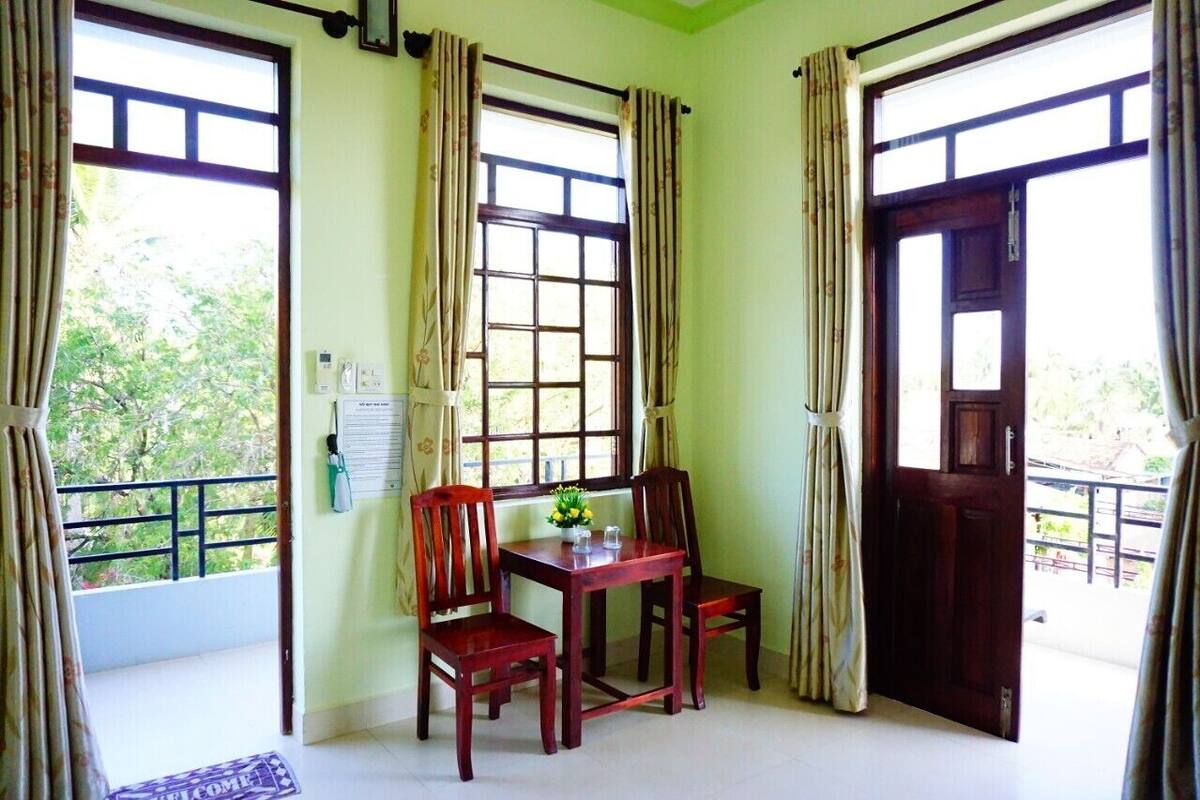 A room with a wooden table and chairs, a window with a view of greenery, and a door.