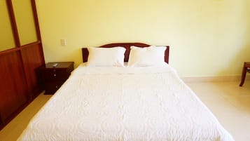 Een net opgemaakt bed met een witte deken in een kamer met houten meubels en lichtgele muren.