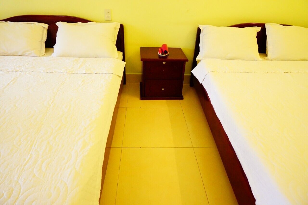 A room with two beds, a nightstand, and a yellow wall.