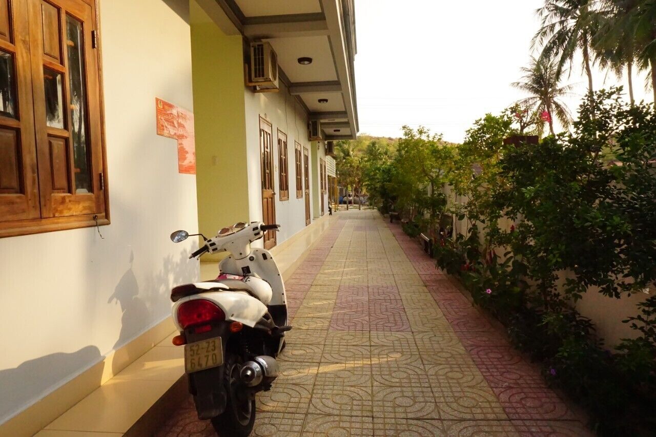 Un pasillo estrecho con una scooter estacionada a la izquierda, un suelo de baldosas y una pared con ventanas y una puerta.