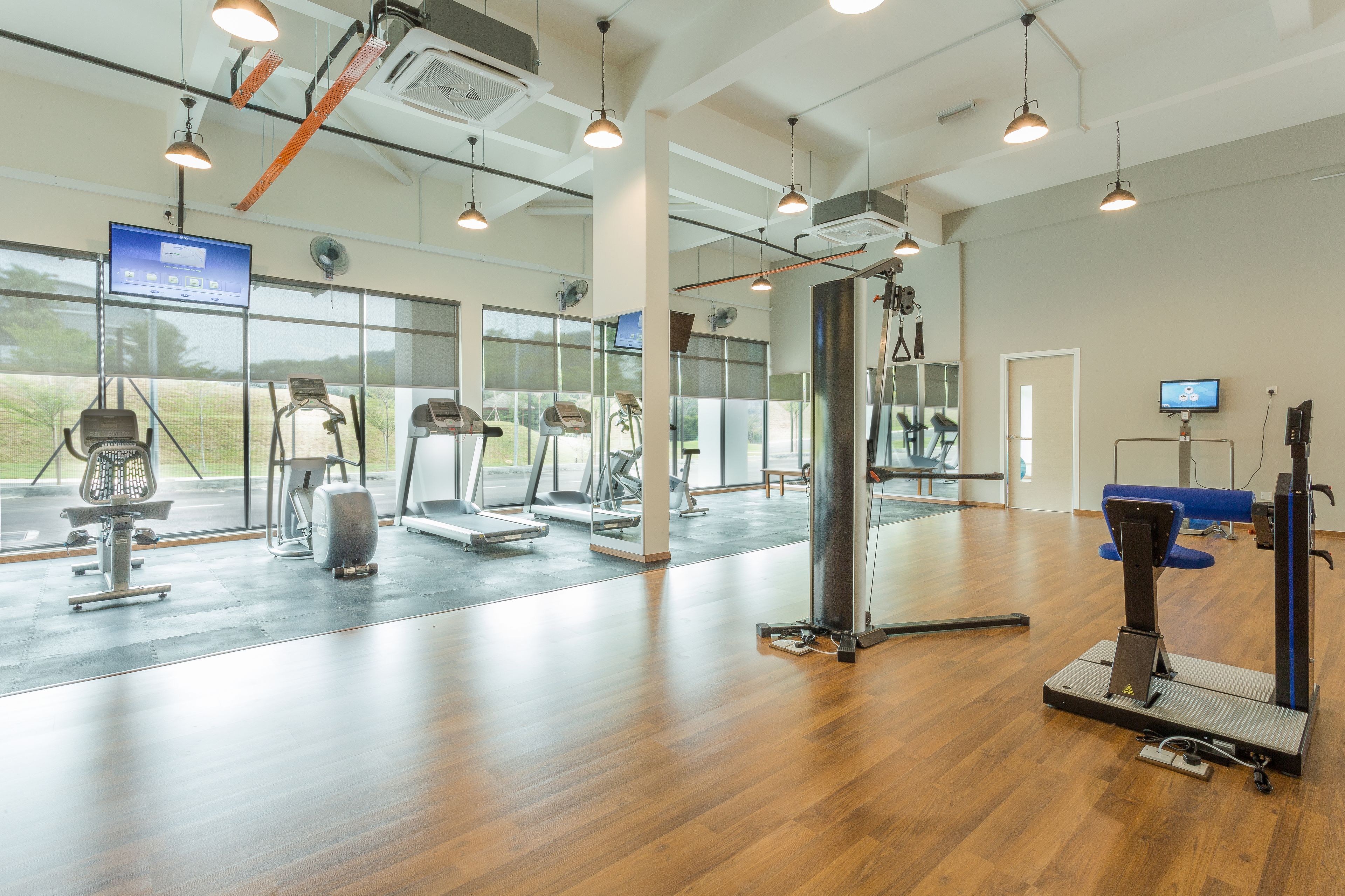 A spacious gym with various exercise equipment, large windows, and a modern design.