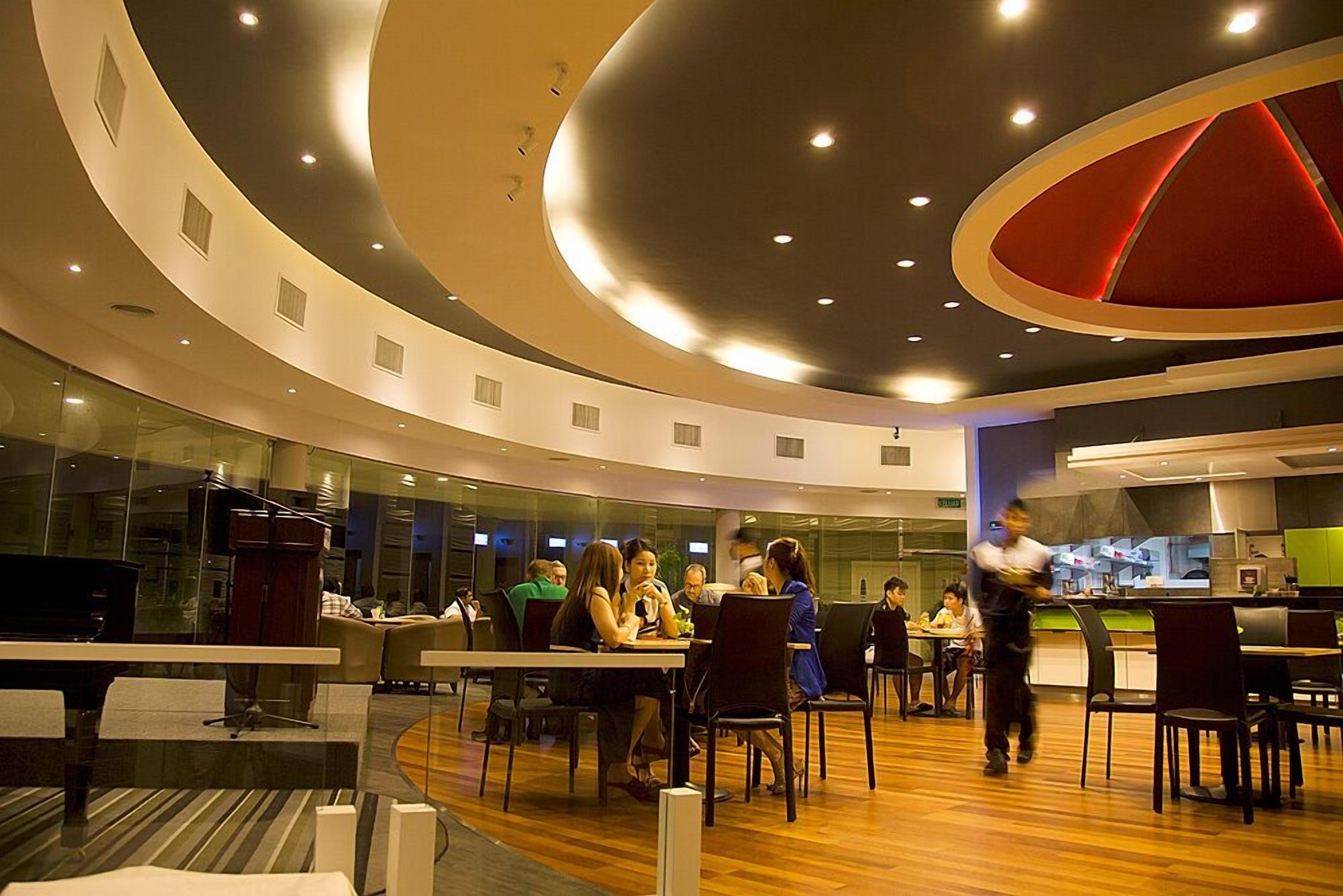 A modern dining area with round tables and chairs, a visible kitchen area, and a curved ceiling design.