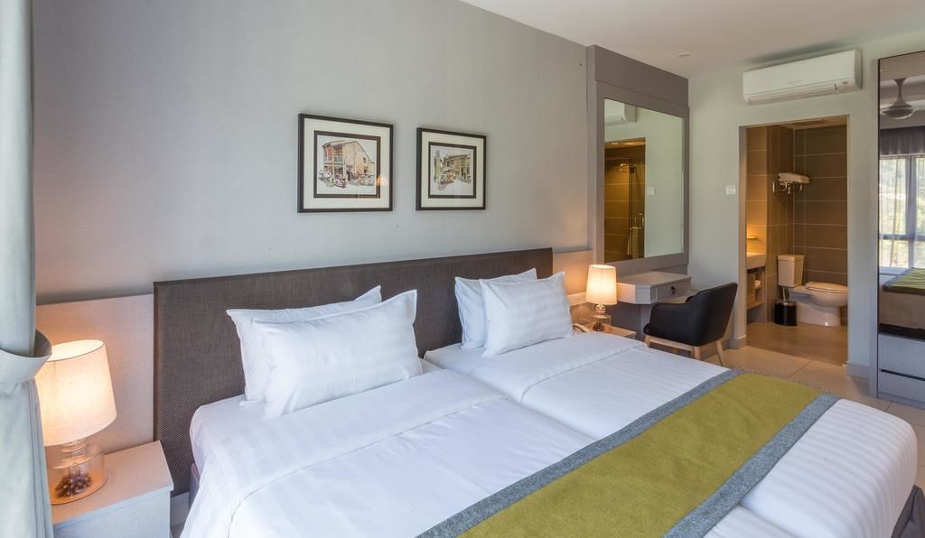 A hotel room with a large bed, two bedside tables with lamps, a desk, a chair, a bathroom, and two framed pictures on the wall.