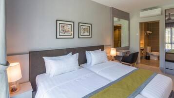 A hotel room with a large bed, two bedside tables with lamps, a desk, a chair, a bathroom, and two framed pictures on the wall.