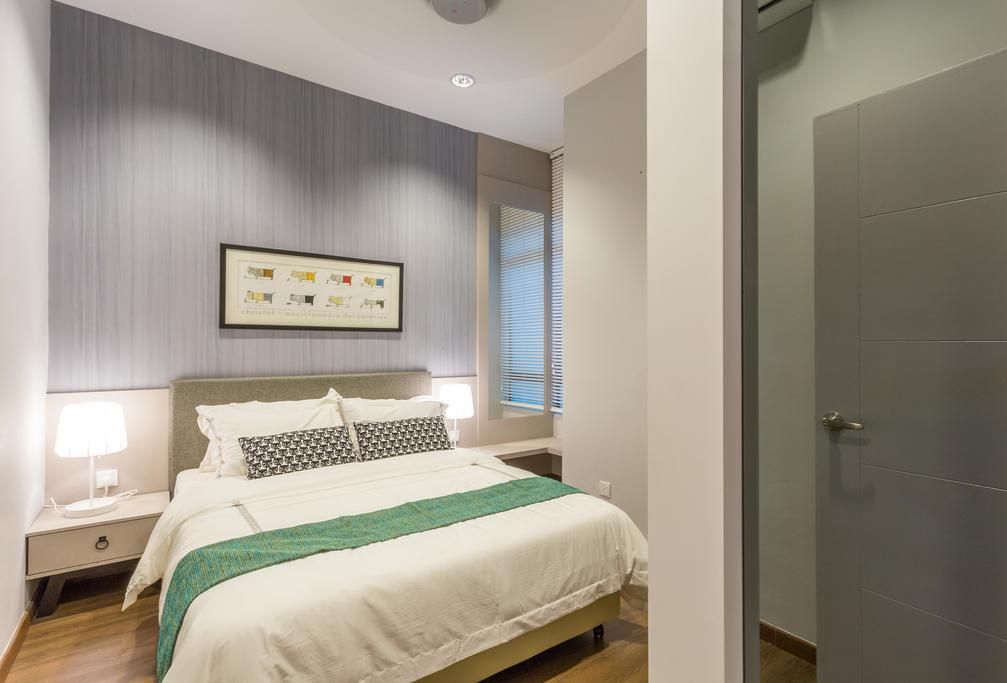 A neatly arranged bedroom with a bed, bedside lamps, a framed picture on the wall, and a door to the right.