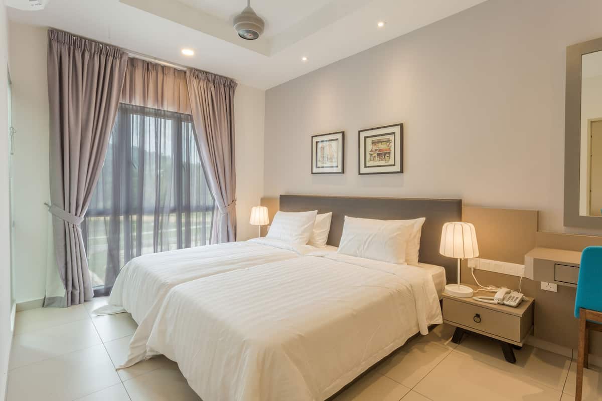 Une chambre d’hôtel avec deux lits, une table de chevet avec une lampe, un bureau avec une chaise et une grande fenêtre avec des rideaux.