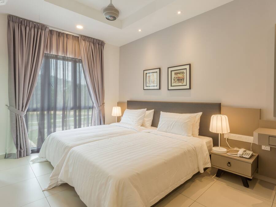 A hotel room with two beds, a nightstand with a lamp, a desk with a chair, and a large window with curtains.
