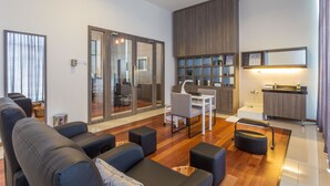 Un salon moderne comprenant un canapé, des poufs, un coin repas et une petite cuisine.