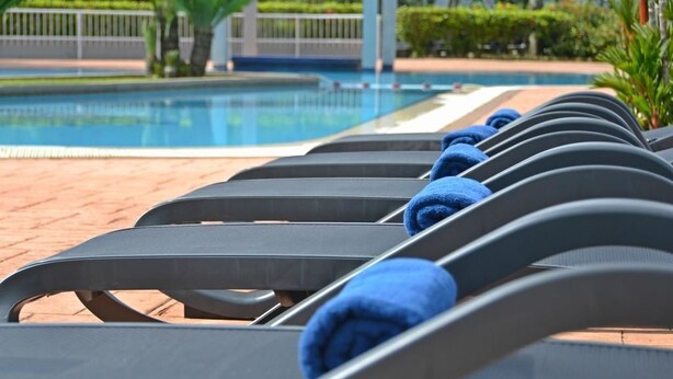 Une rangée de chaises longues avec des serviettes bleues, une piscine et un chemin en briques.