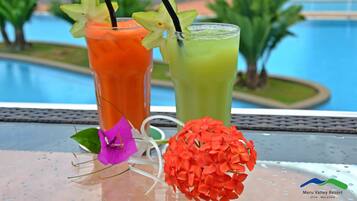 Two cocktails with straws and a decorative flower on a table by a poolside.