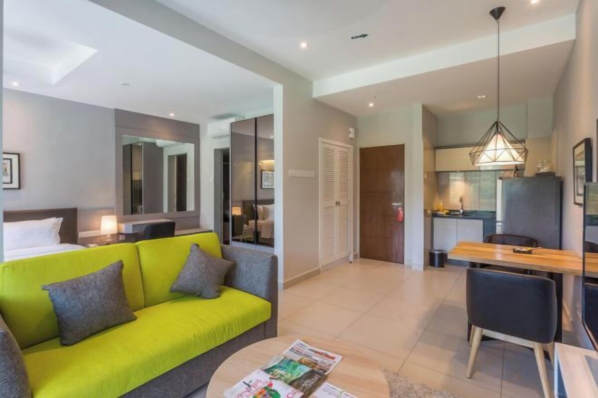 A modern hotel room with a sofa, a dining table, a kitchen area, and a separate sleeping area.