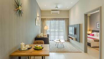 A modern hotel room with a dining area, a sofa, a TV, and a bed.