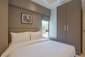 Un dormitorio con una cama grande, cabecera, armario y ventana con vistas a zonas verdes.