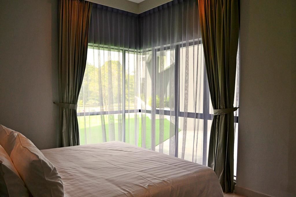 A bedroom with a large bed, sheer curtains, and a view of a green lawn.