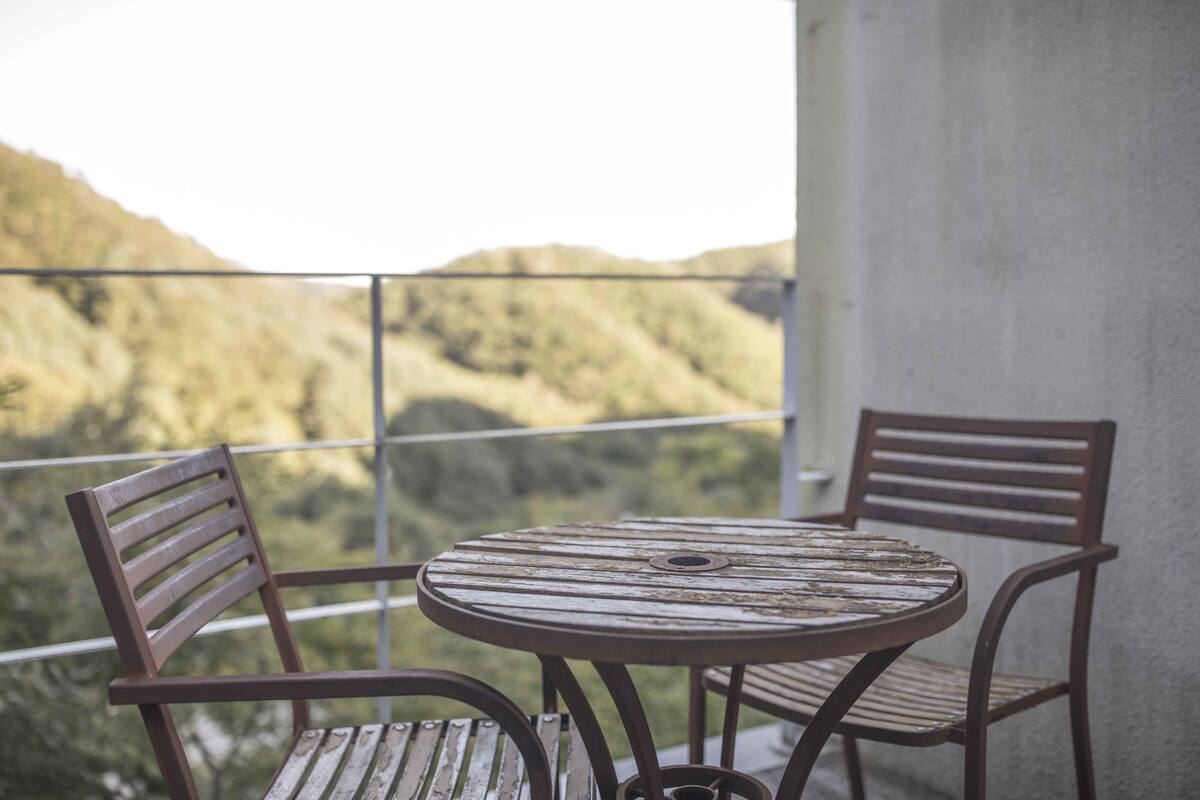 A balcony with a round metal table and two wooden chairs.