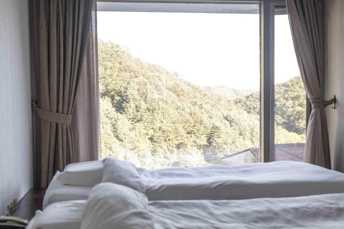 A bed with white linens in a room with a large window.