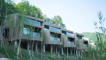 A modern multi-story building with balconies, surrounded by trees and greenery.