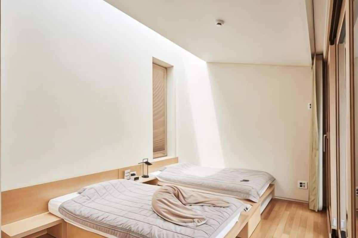 A modern bedroom with two beds, a small bedside table, a window, and a door.