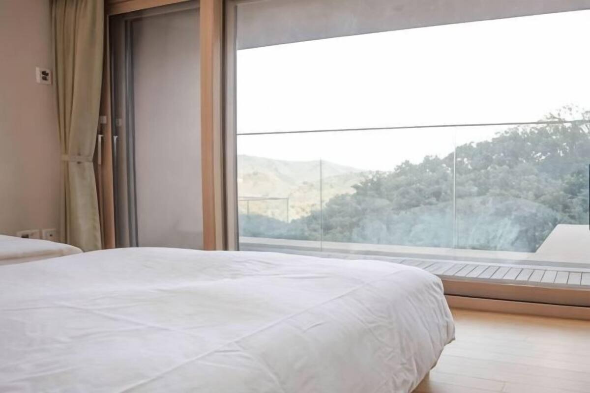 A bedroom with a large window, a bed, and a view of a mountainous landscape.