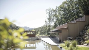 Ein ruhiger Poolbereich im Freien mit einem Kiesweg, einem hölzernen Pavillon und einem Gebäude mit flachem Dach.