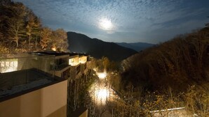 Ein Nachtblick auf einen Berg mit klarem Himmel und vollem Mond. Ein Gebäude mit einem Glasbalkon blickt auf einen beleuchteten Weg.