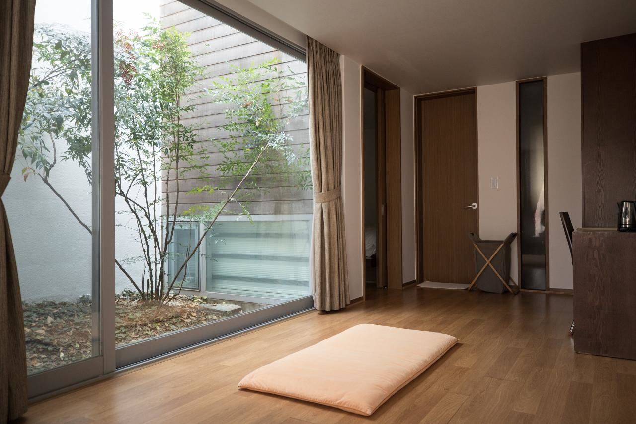 A modern room with a large sliding glass door leading to a garden, a wooden floor, and a minimalist design.