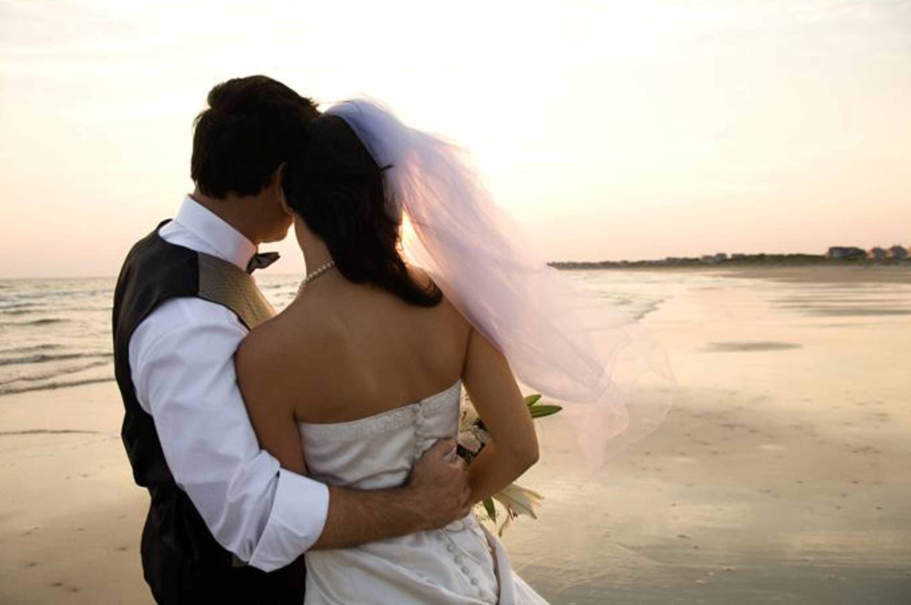 A couple embracing on a beach with a sunset in the background.