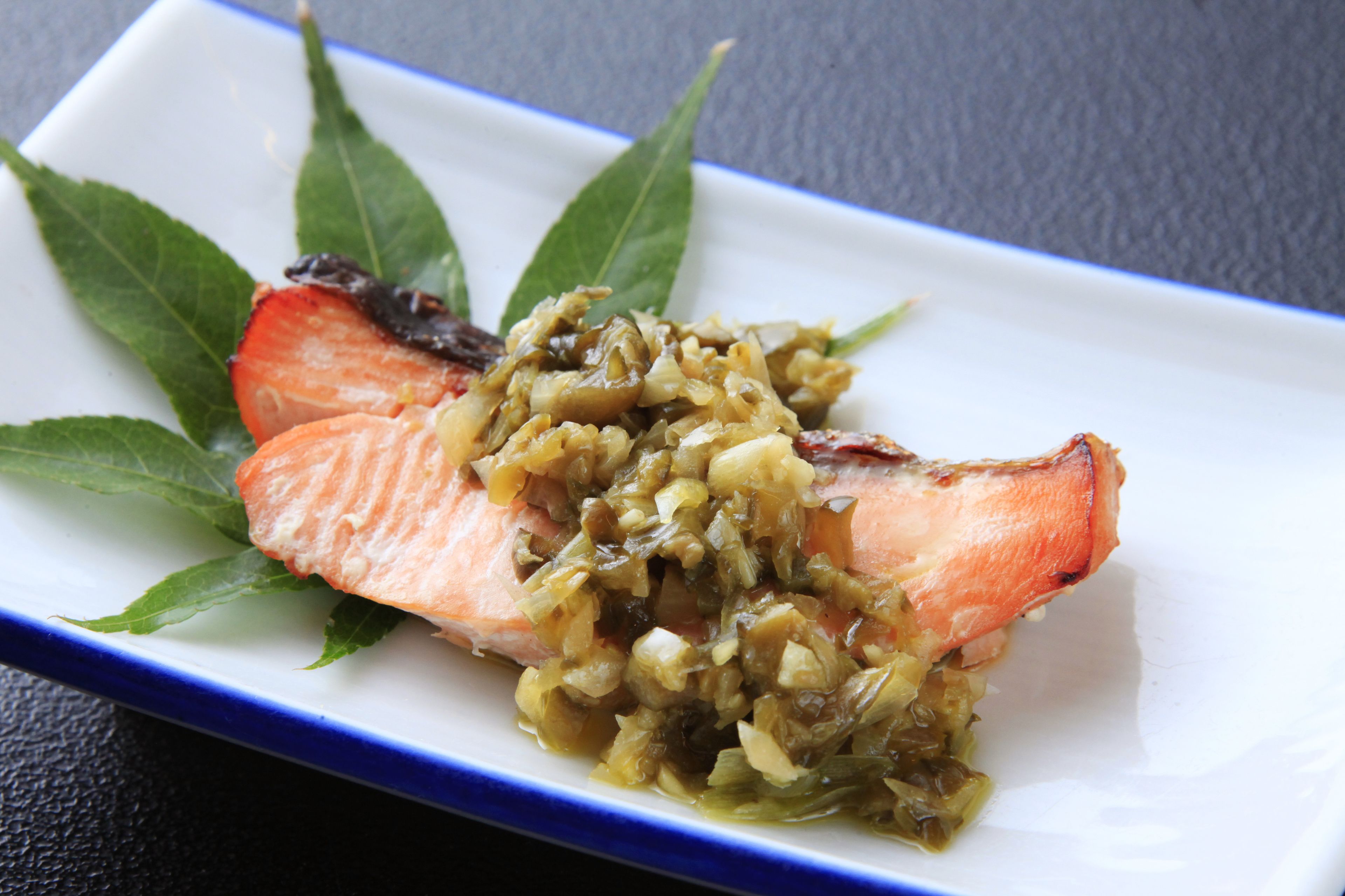A plate with salmon and a green sauce, garnished with leaves.