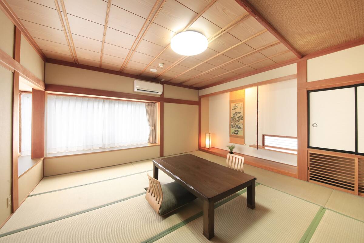 A traditional Japanese room with tatami flooring, a wooden table, a sliding door, and a window with curtains.