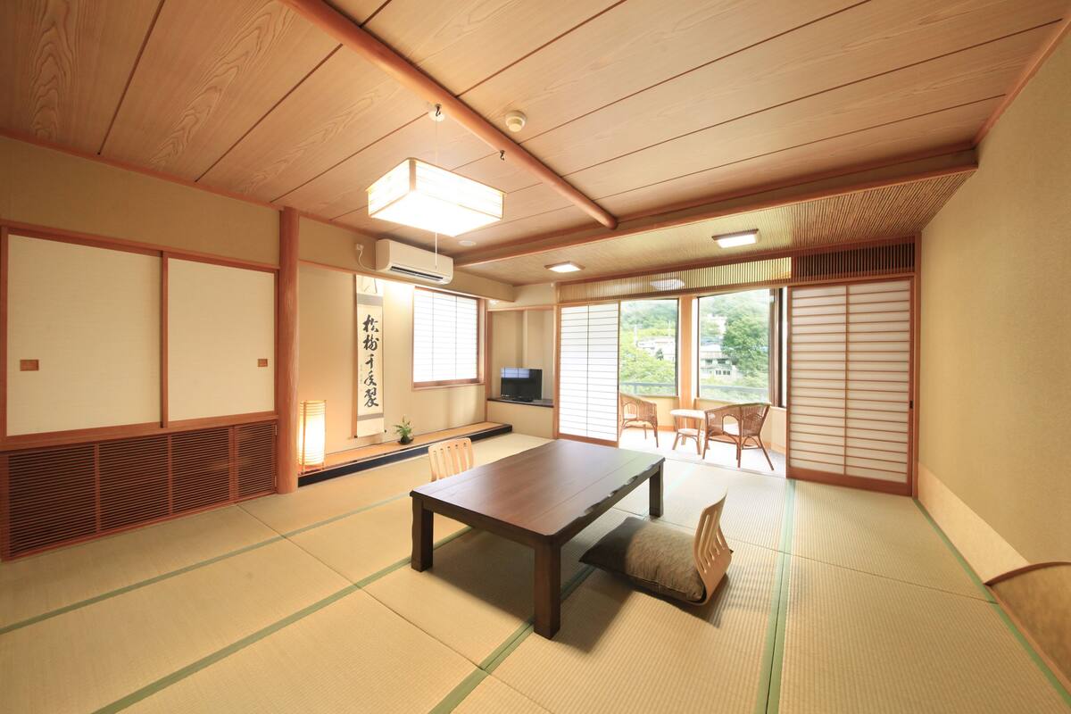 A traditional Japanese room with tatami flooring, a low table, sliding doors, and a TV.