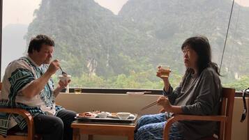 Dos personas cenando en una mesa con una bandeja de comida y bebidas, con vistas a un paisaje montañoso.