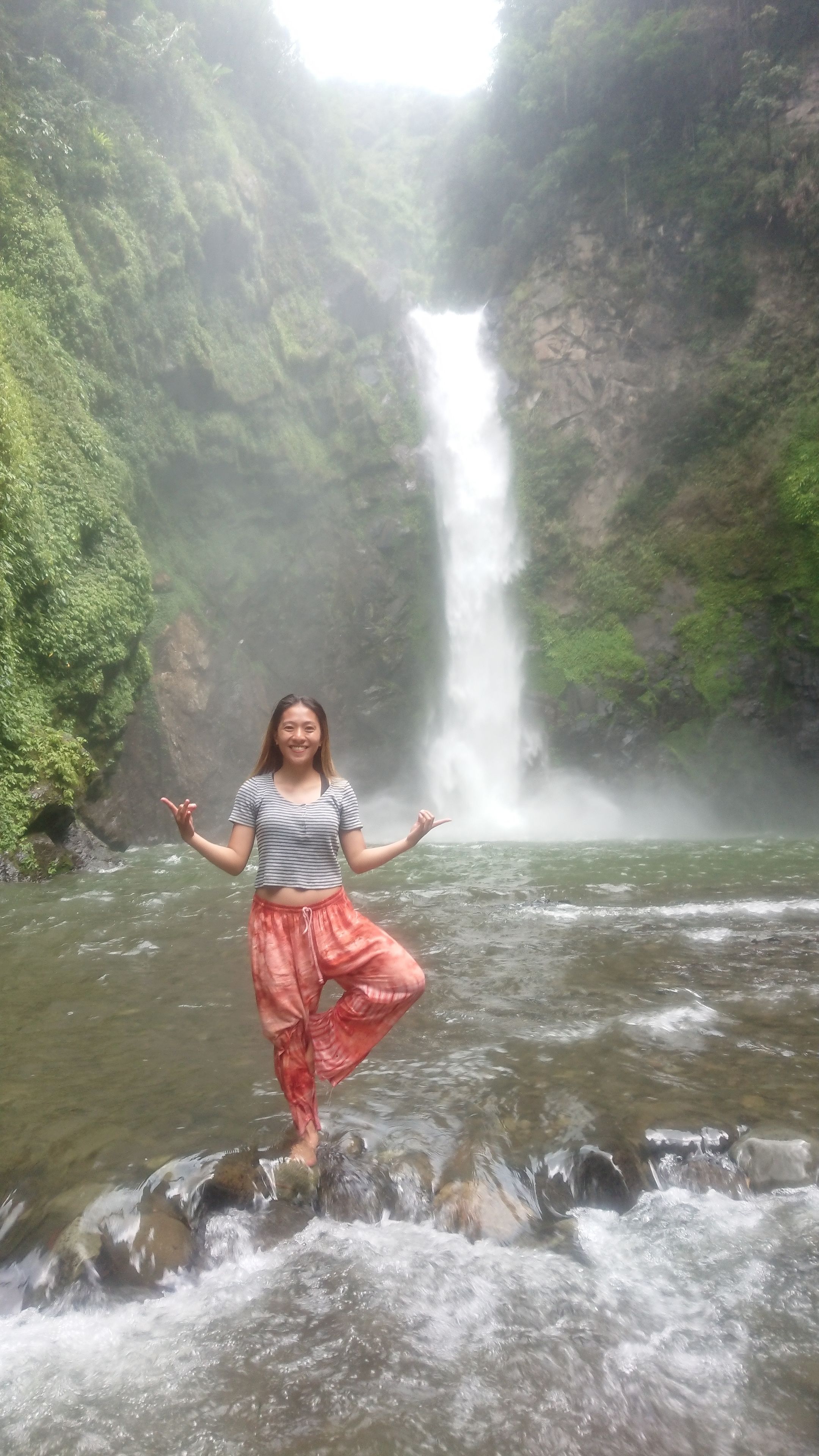 A person standing in a river with a waterfall in the background.