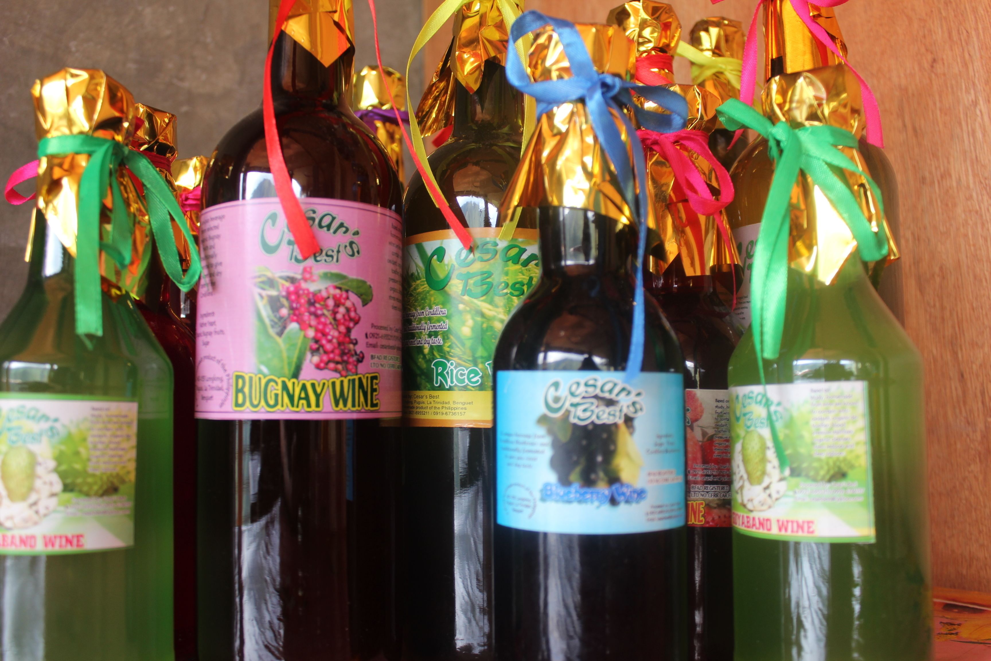Plusieurs bouteilles de vin, décorées de rubans et d’étiquettes colorées, dont les marques « Bugnay Wine » et « Cesar’s Best ».