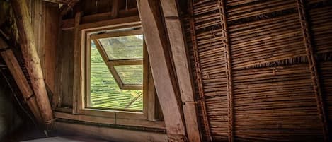 A rustic attic bedroom with a slanted roof, a large window, and wooden beams.