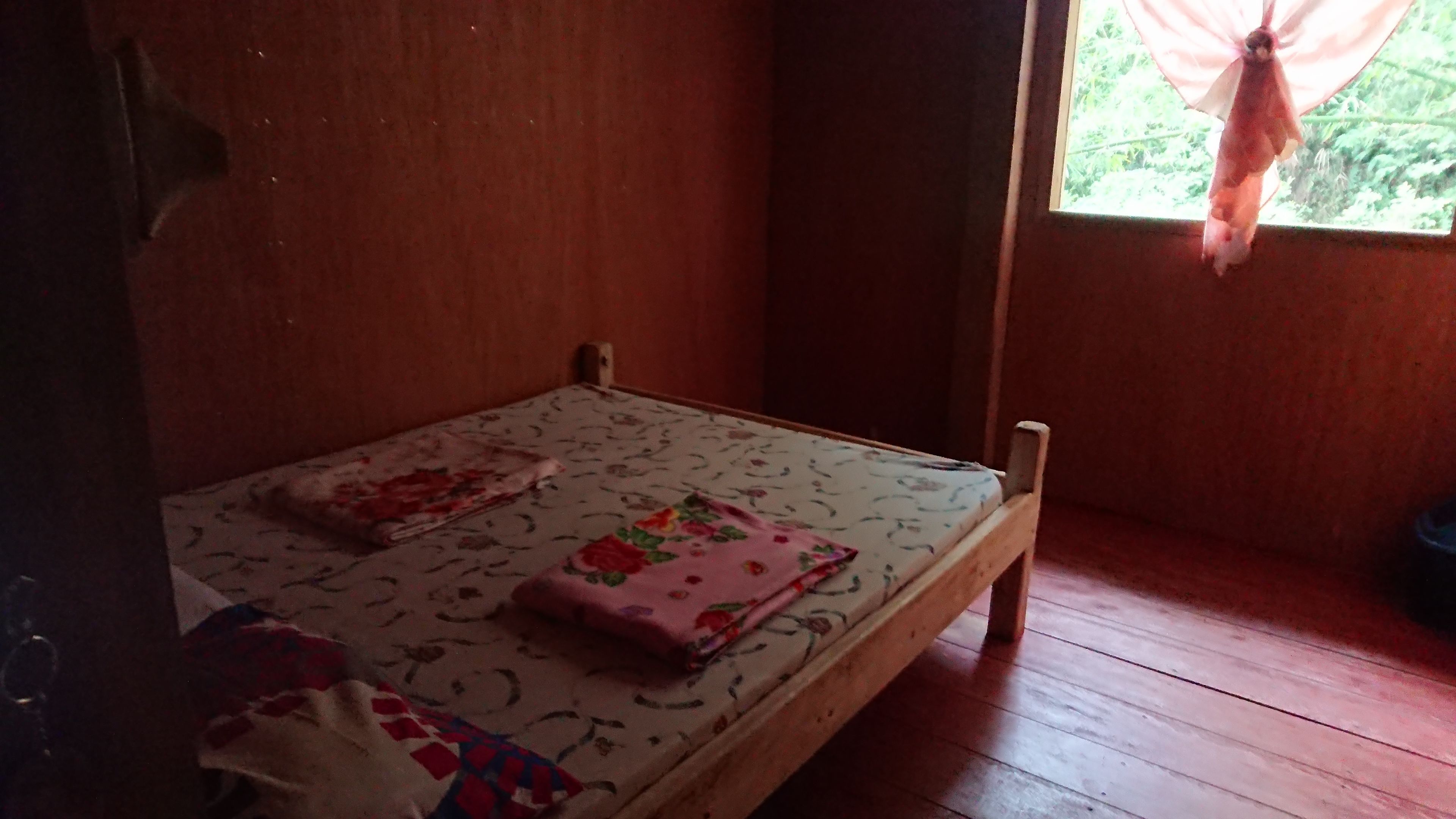 A small, single-bed room with a wooden floor and a window with a curtain.