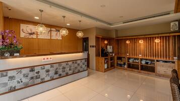 A hotel reception area with a wooden reception desk, information board, and a seating area with wooden paneling.