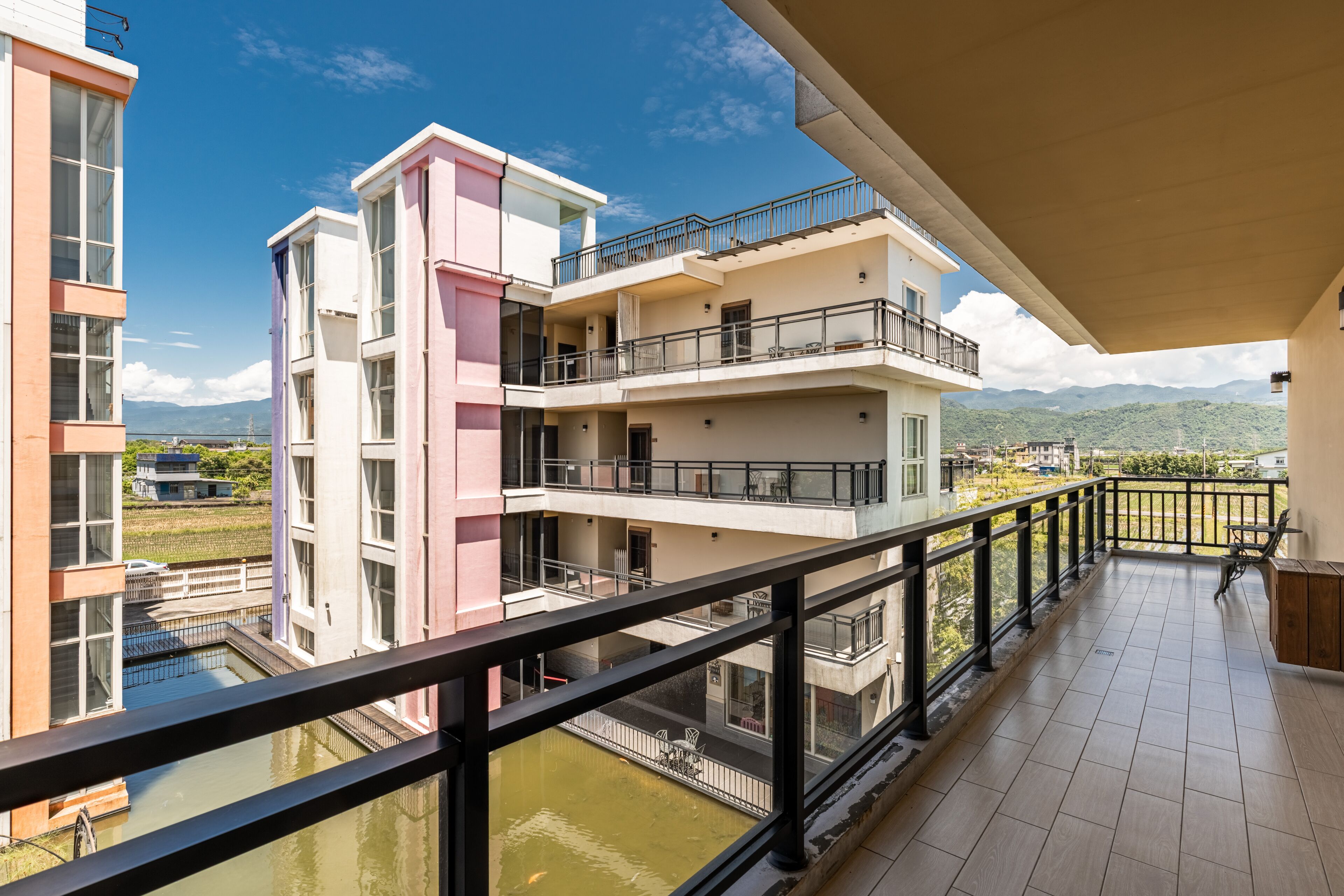 A multi-story building with balconies, a view of a river, and mountains in the distance.