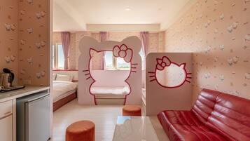 A room with a bed, a red leather sofa, a small table, and a kitchen area with a kettle.
