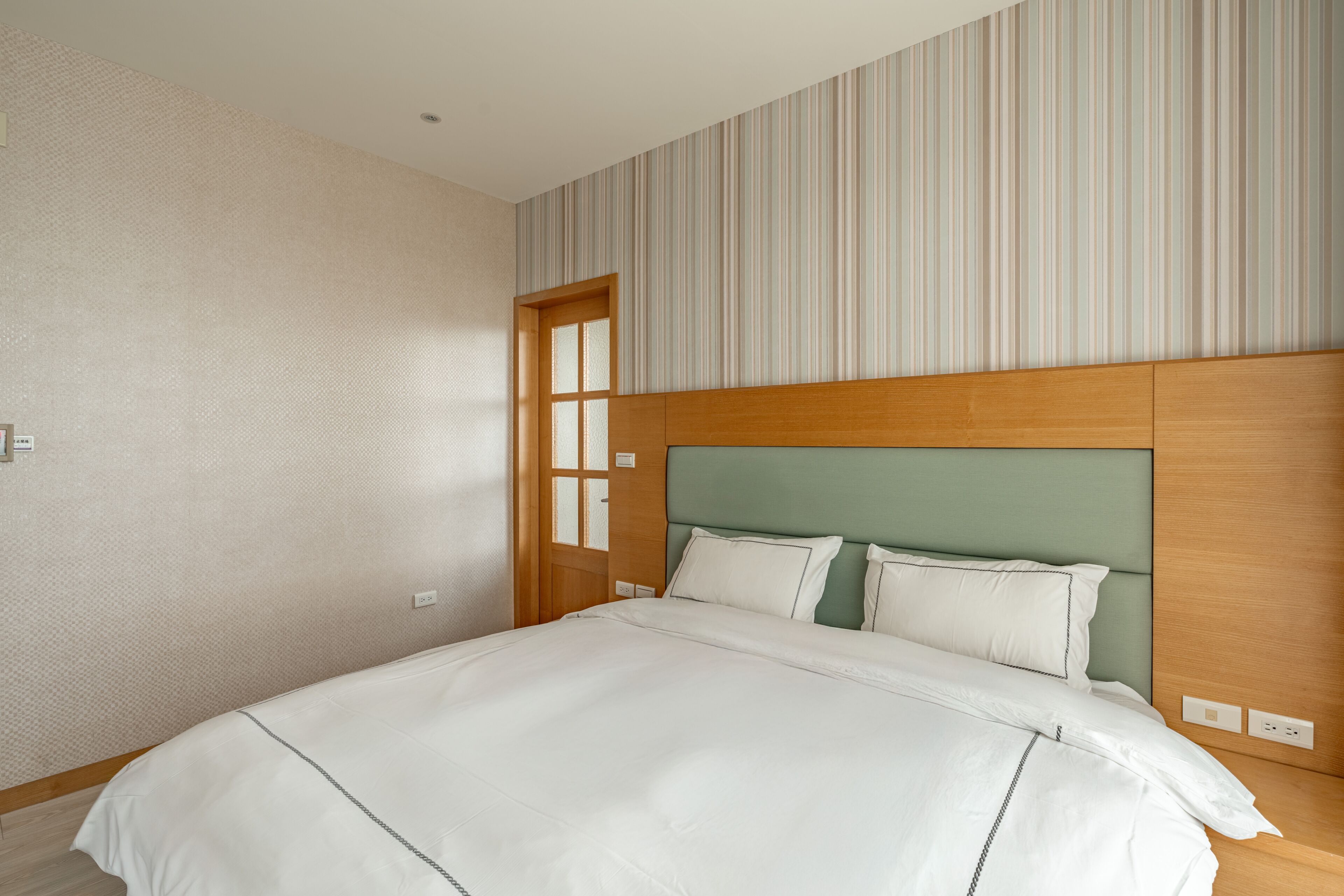 A hotel room with a large bed, a wooden headboard, and a striped wall.