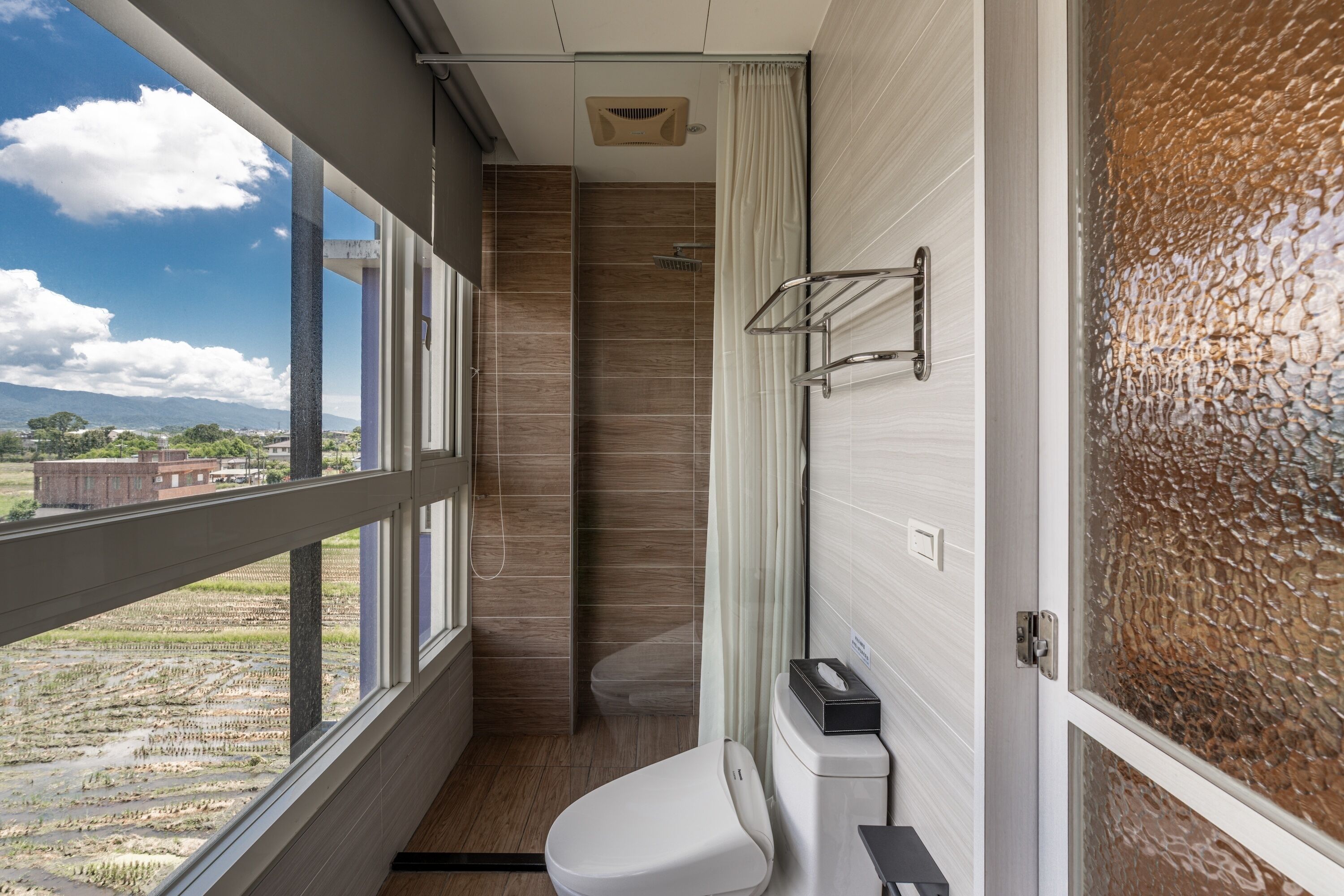 A modern bathroom with a toilet, shower, and a window offering a view of the outdoors.