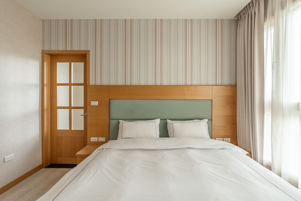 Habitación de hotel con cabecera de madera, cama con ropa de cama blanca, pared a rayas y puerta con paneles de vidrio esmerilado.
