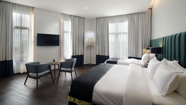 Una habitación de hotel con una cama grande, dos sillas, un televisor y una lámpara.