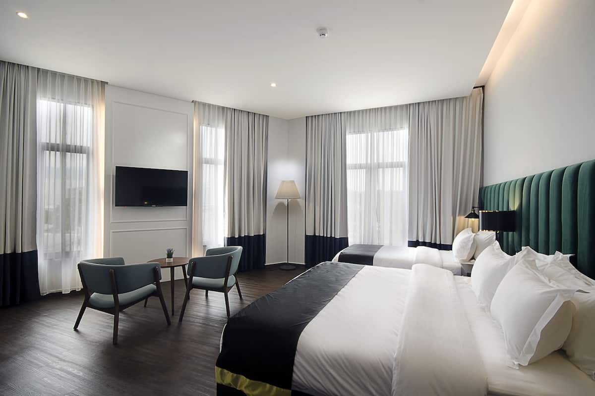 A hotel room with a large bed, two chairs, a TV, and a lamp.